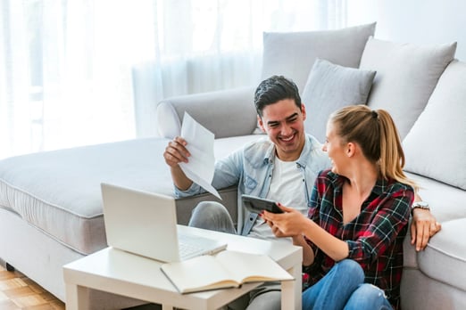 A cheerful young couple in their home using a laptop to analyze their finances for taking out an RRSP loan.