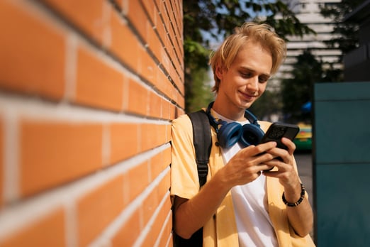 A young caucasian man leaning on a brick wall and checking his RBC High Interest eSavings account balance on a smartphone.