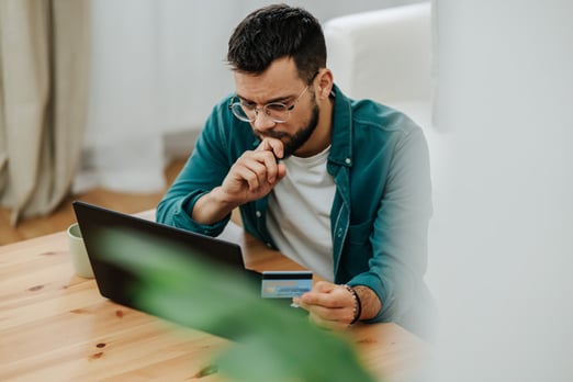 Person looking at laptop while holding credit card