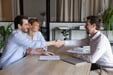 A confident bank associate meeting and shaking hands with happy couple.