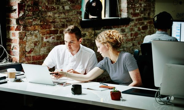 Man and woman look at laptop screen together at desk