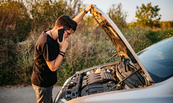 Adult looking at open hood of car and calling roadside assistance