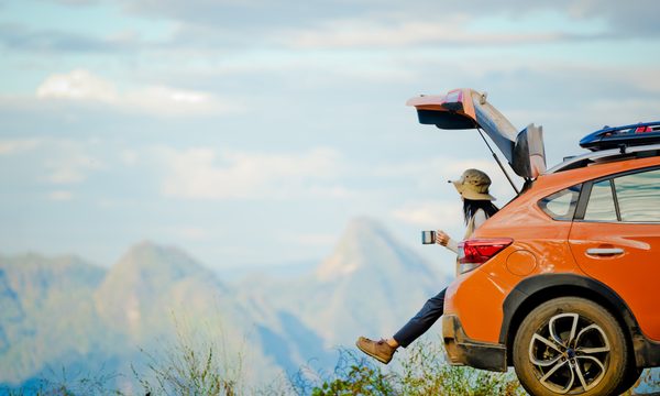 Woman sitting on car tailgate and looking at mountains