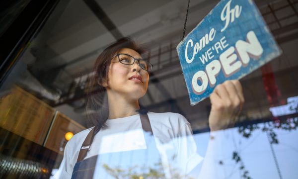 Portrait of a happy Asian business owner hanging an open sign on the door at a Cafe and smiling.