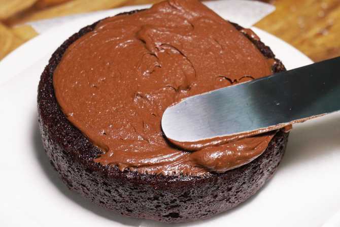 spreading frosting on a chocolate cake with a spatula